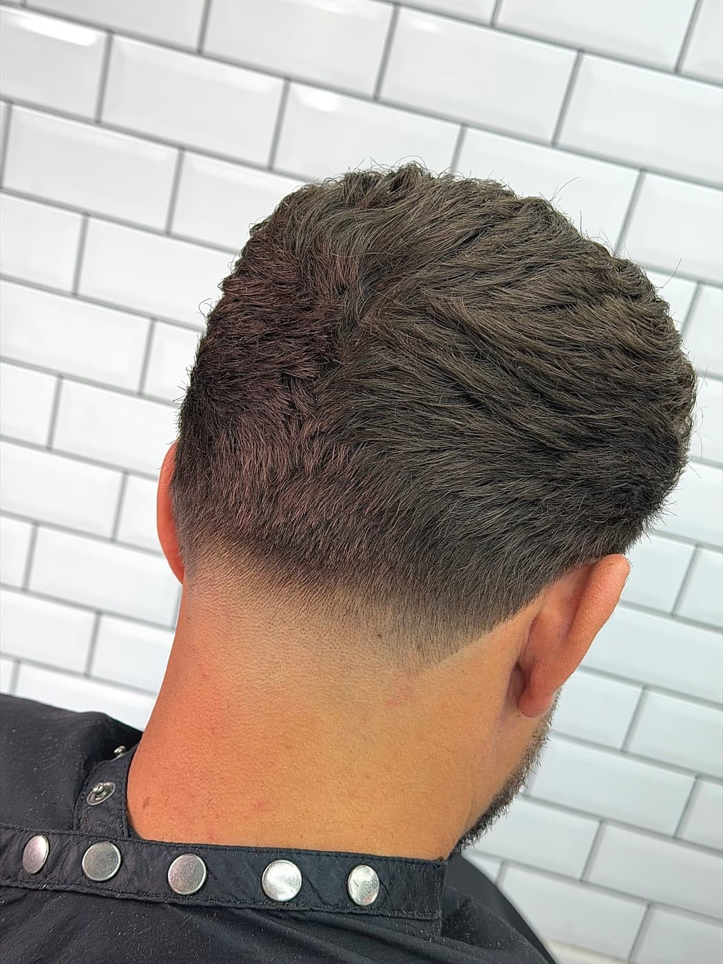 Back view of a textured crop with a clean taper fade at the neckline, against the shop's white subway tiles